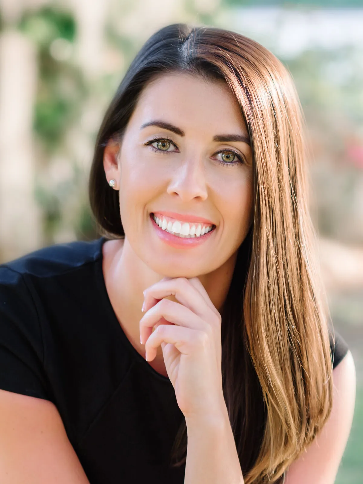 Professional headshot of a smiling woman with long straight brown hair in a black top with her hand at her chin by Myrtle Beach headshot photographer Pasha Belman