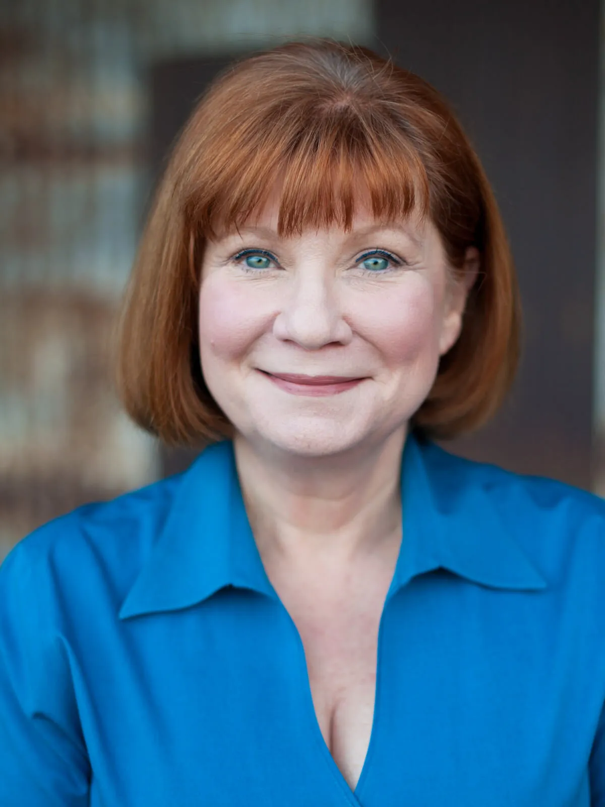 Professional headshot of a smiling woman with auburn hair and bangs in a bright blue blouse by Myrtle Beach headshot photographer Pasha Belman
