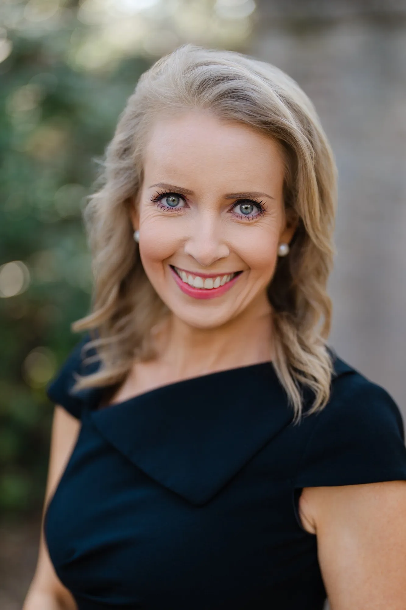 Professional headshot of a woman with wavy blonde hair in a navy dress with a sculpted neckline, outdoors by Myrtle Beach headshot photographer Pasha Belman