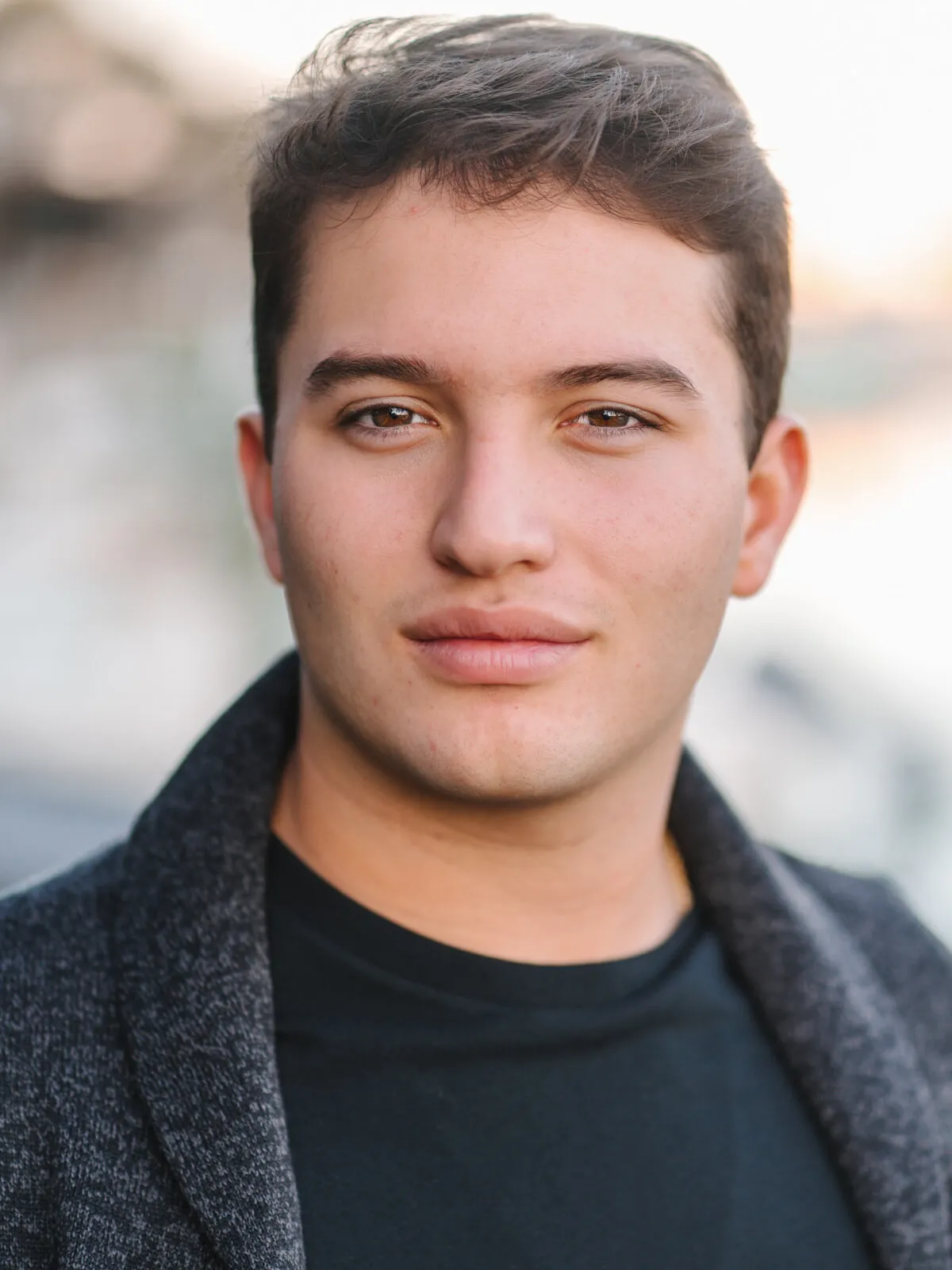 Professional headshot of a young man with short brown hair in a dark jacket over a black t-shirt, by the beach by Myrtle Beach headshot photographer Pasha Belman