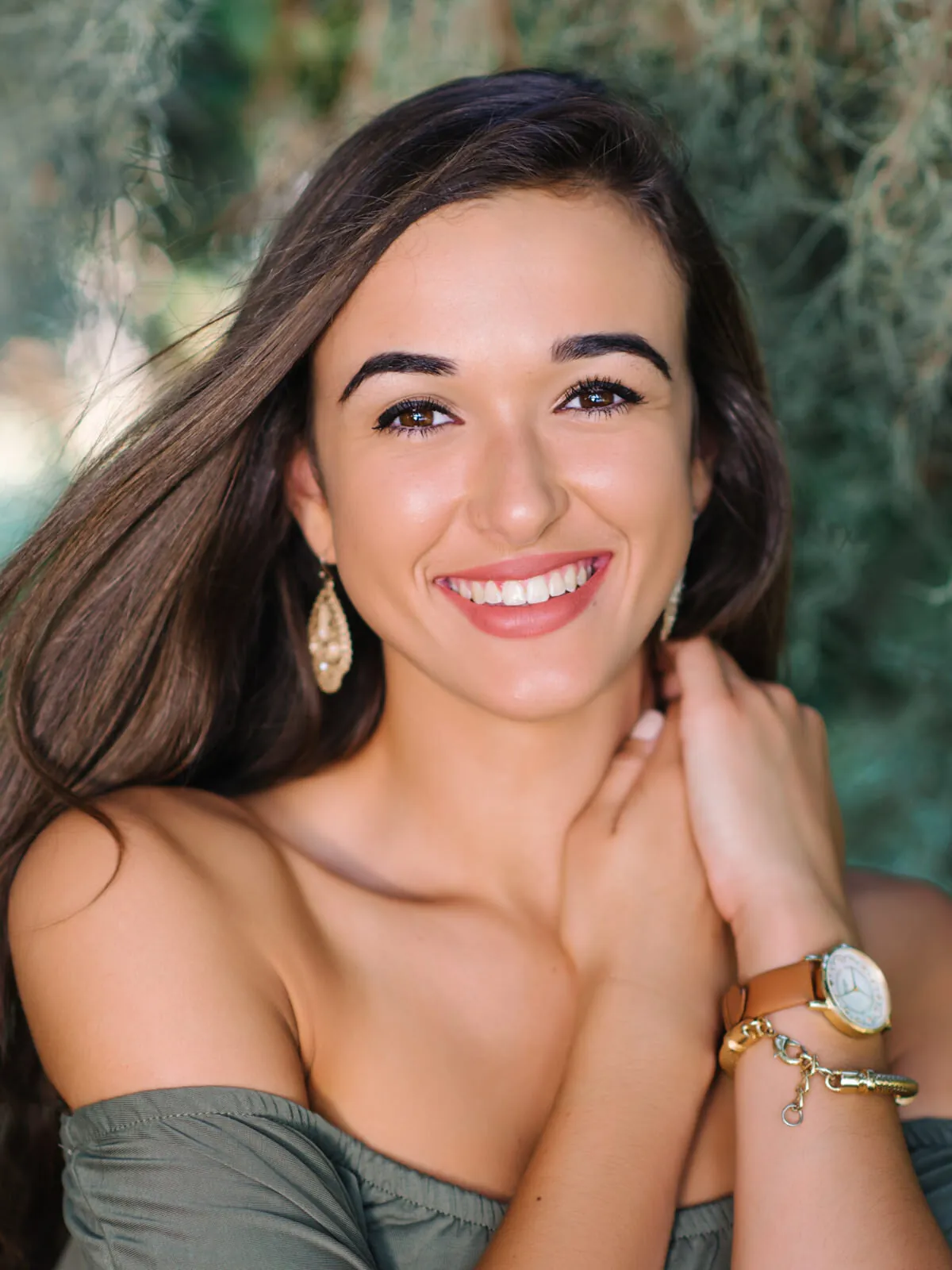 Professional headshot of a smiling young woman with long brown hair, drop earrings and a watch in an olive off-shoulder top by Myrtle Beach headshot photographer Pasha Belman