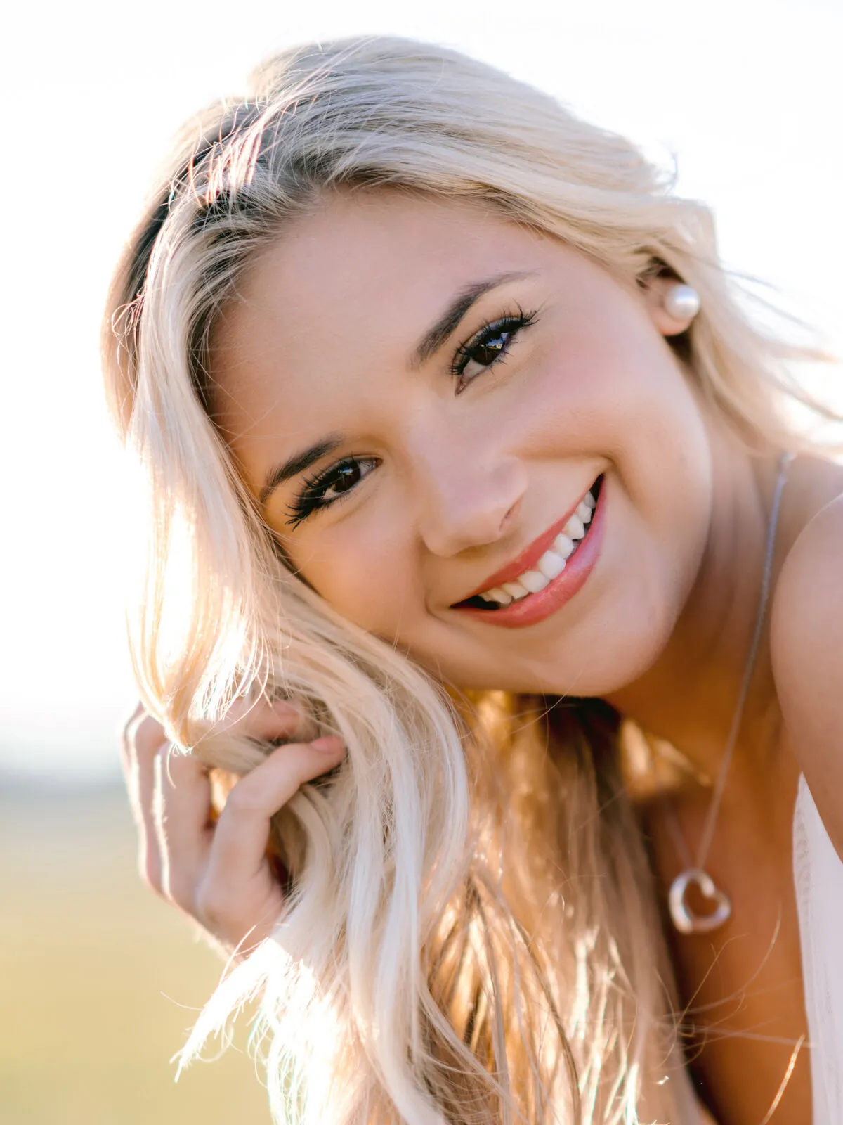 Professional headshot of a young woman with long blonde hair smiling with one hand in her hair, backlit by warm light by Myrtle Beach headshot photographer Pasha Belman