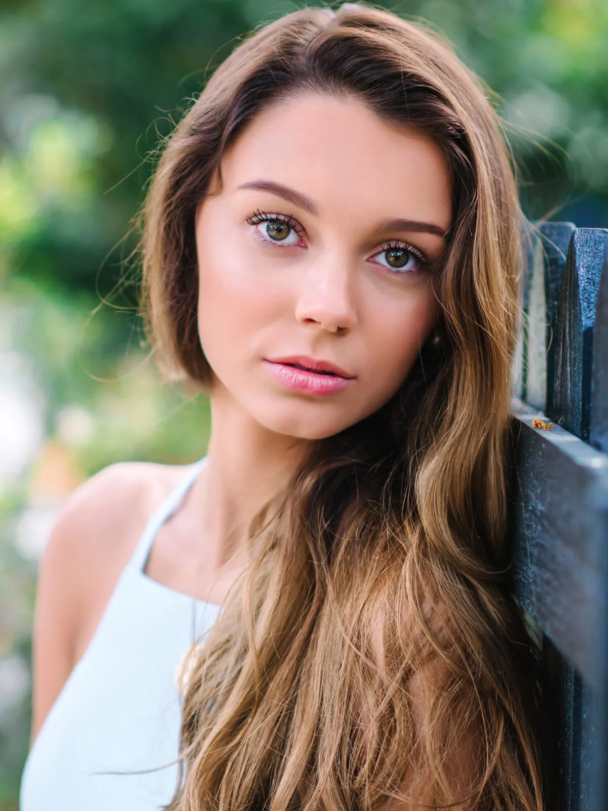 Professional headshot of a young woman with long brown hair in a white top in front of a dark iron gate by Myrtle Beach headshot photographer Pasha Belman