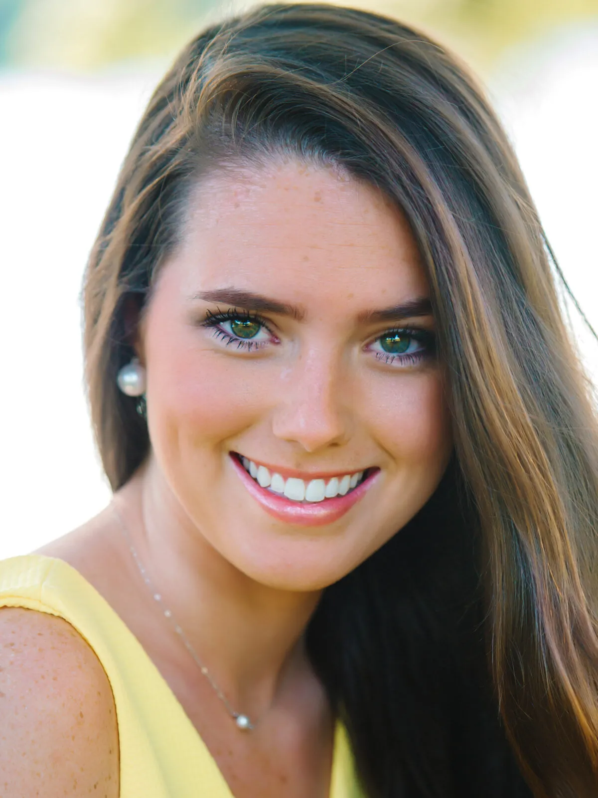 Professional headshot of a smiling young woman with freckles, light eyes and long hair in a yellow top by Myrtle Beach headshot photographer Pasha Belman