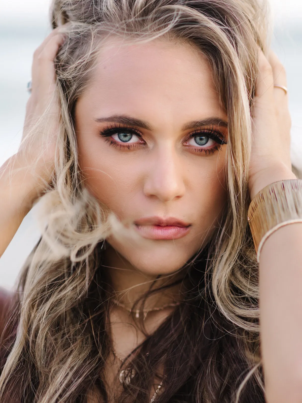 Professional headshot of a young woman with wavy hair and both hands in her hair wearing a gold cuff bracelet by Myrtle Beach headshot photographer Pasha Belman