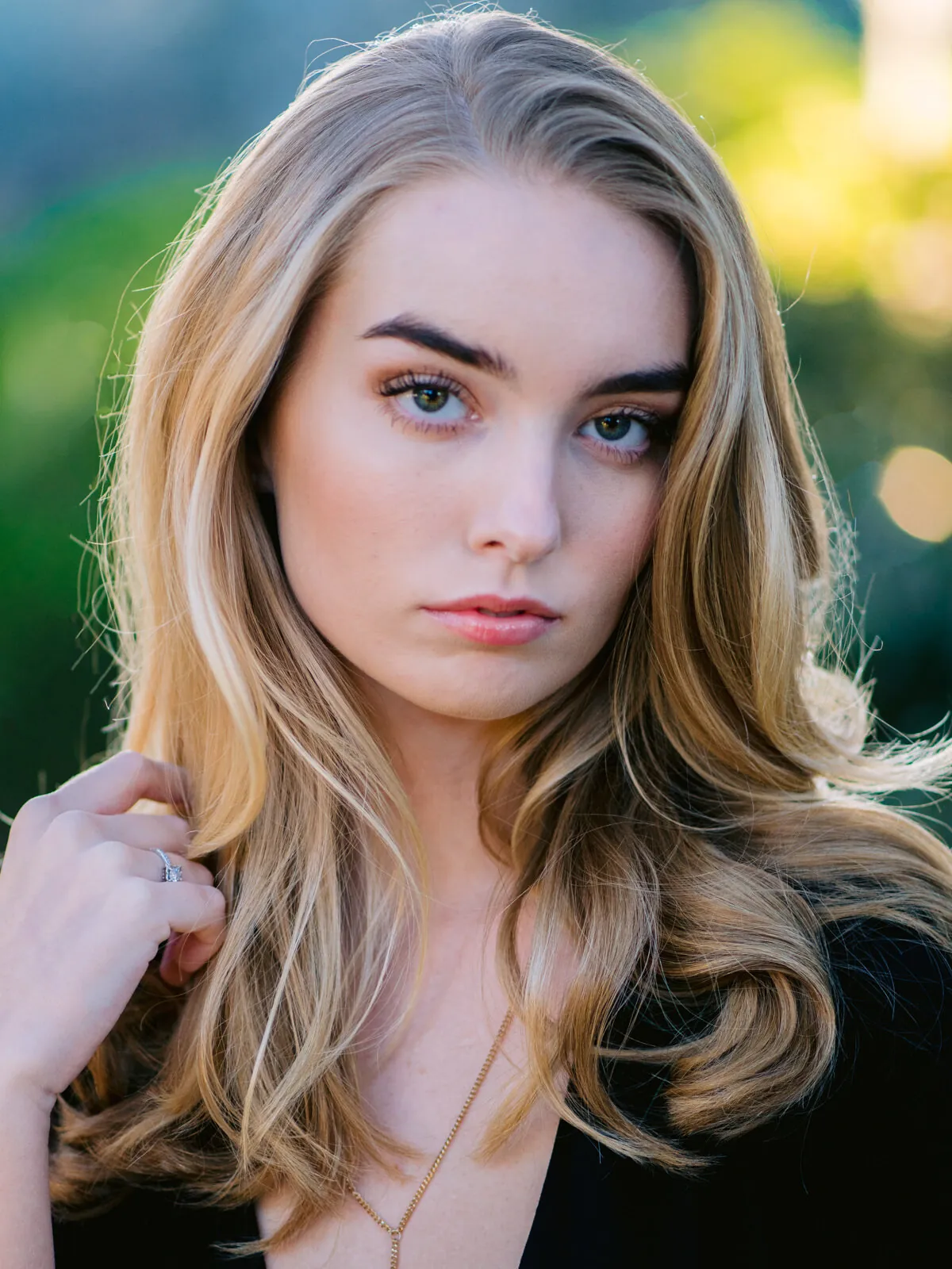 Professional headshot of a young woman with long blonde hair holding a strand of hair, in a black top by Myrtle Beach headshot photographer Pasha Belman