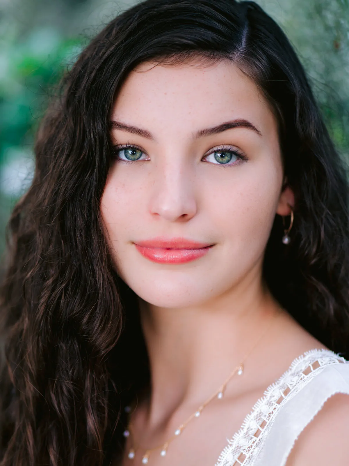Professional headshot of a young woman with long dark wavy hair and bright blue eyes, in a white lace top by Myrtle Beach headshot photographer Pasha Belman