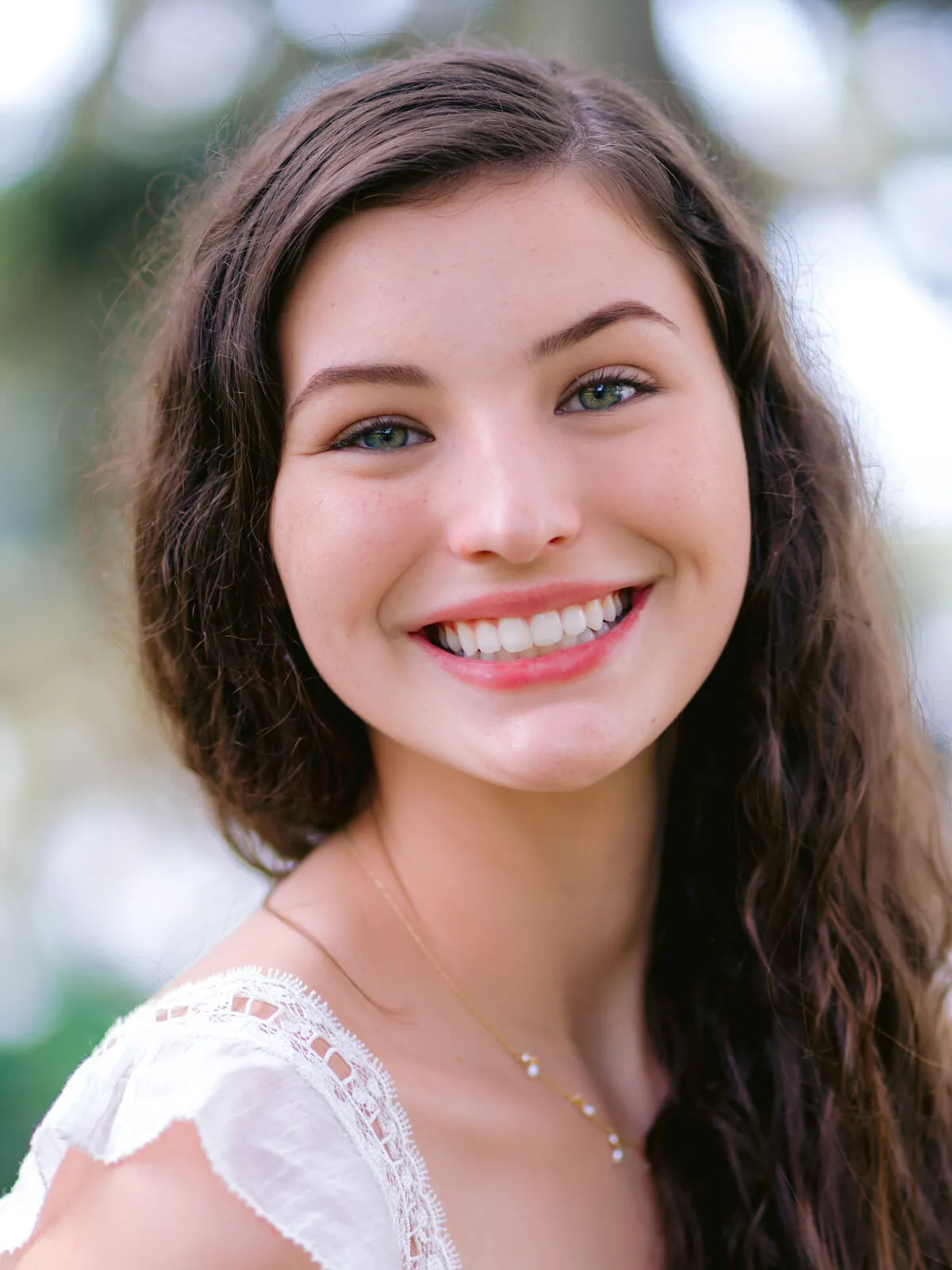 Professional headshot of a smiling young woman with long wavy dark hair in a white lace top by Myrtle Beach headshot photographer Pasha Belman