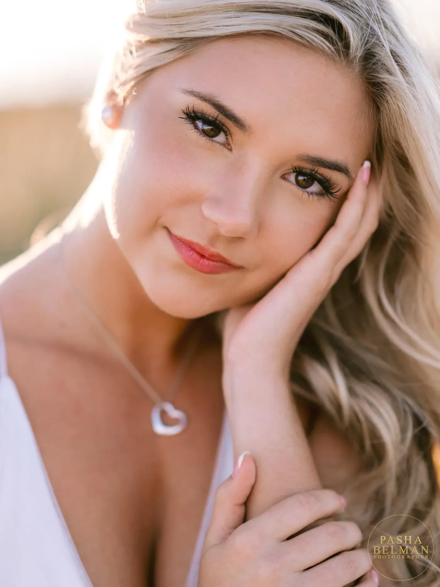 Close-up of a senior girl with her hand on her cheek and a heart necklace in golden hour light