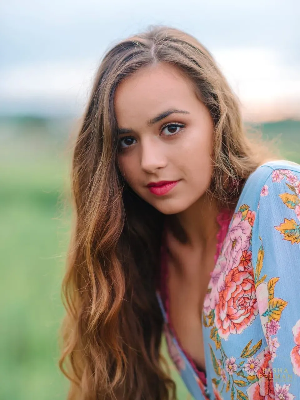Close-up of a smiling senior girl with long wavy hair leaning forward in front of green marsh on Pawleys Island
