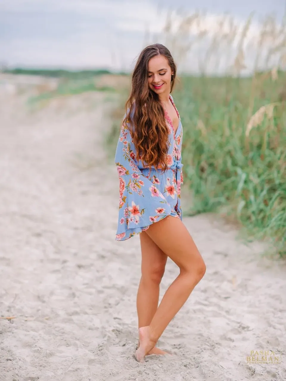 Senior girl in a floral romper posing on a sandy beach path beside sea oats on Pawleys Island