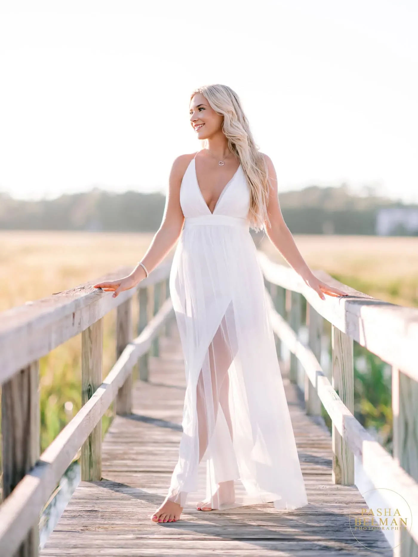 Pawleys Island high school senior in a flowing white dress standing on a weathered boardwalk over the marsh
