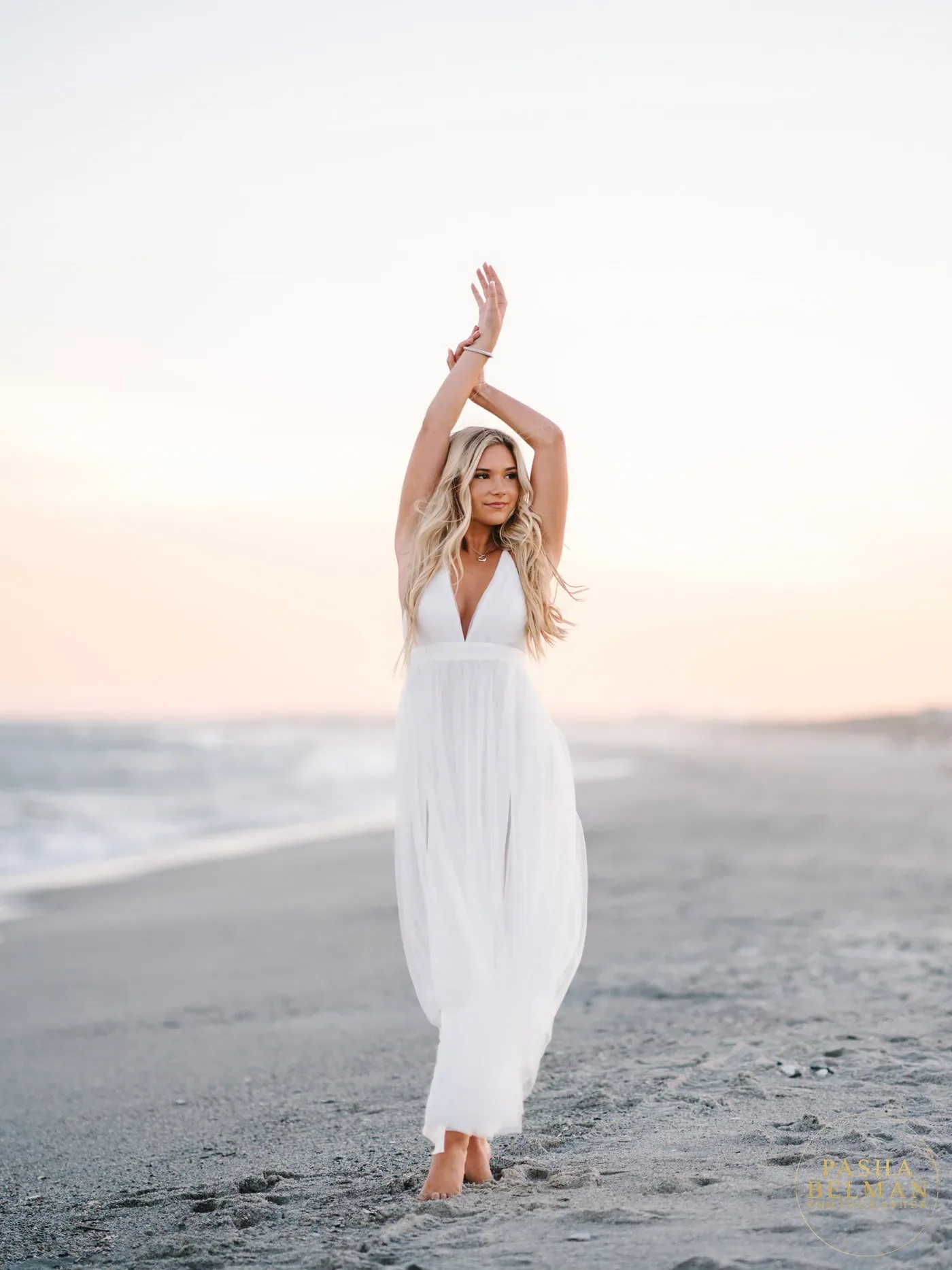 Senior girl in a white dress with her arms raised walking a quiet beach at sunset on Pawleys Island