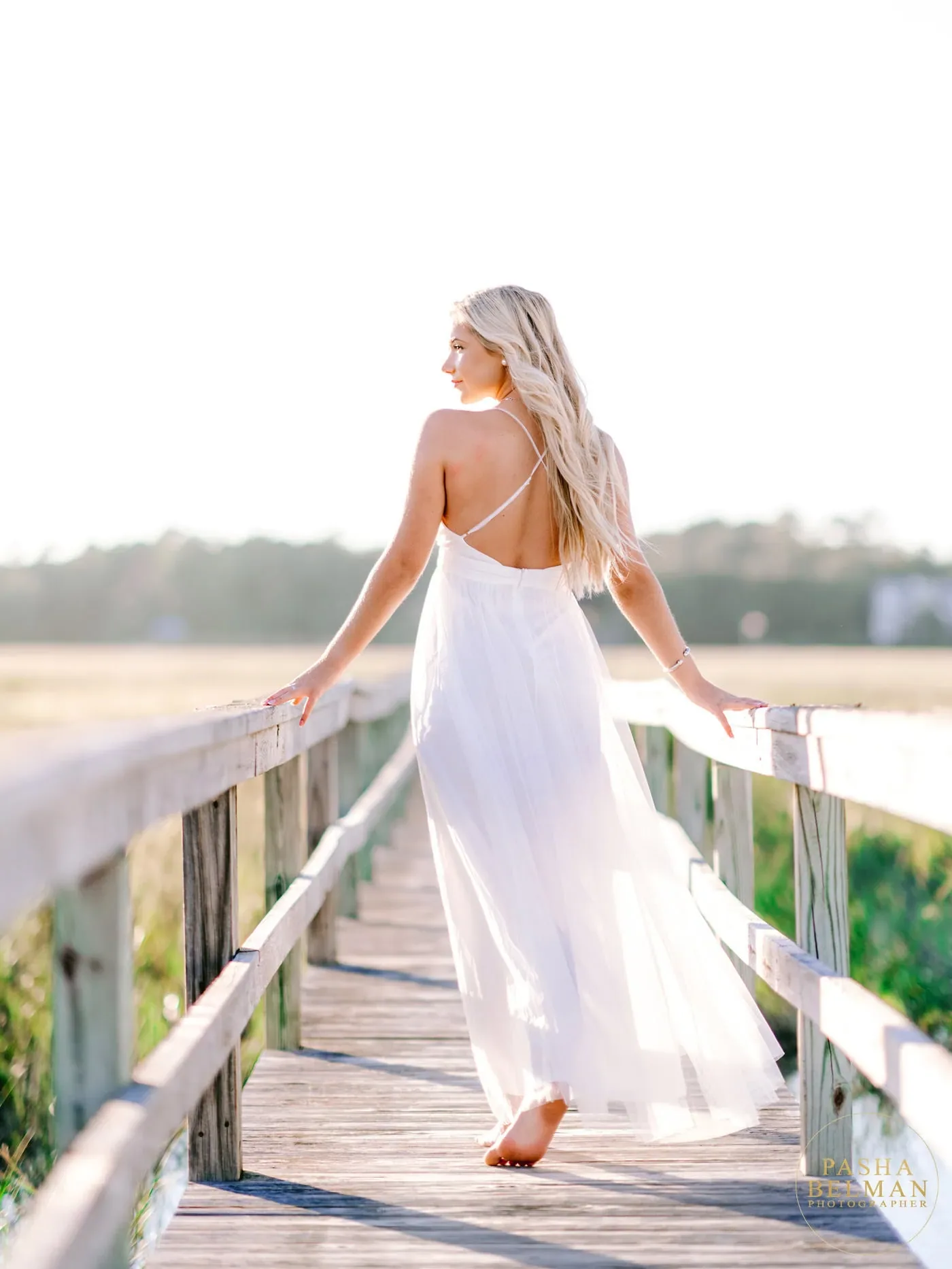 Senior girl in a white dress with crossed back straps walking away on a Pawleys Island marsh boardwalk