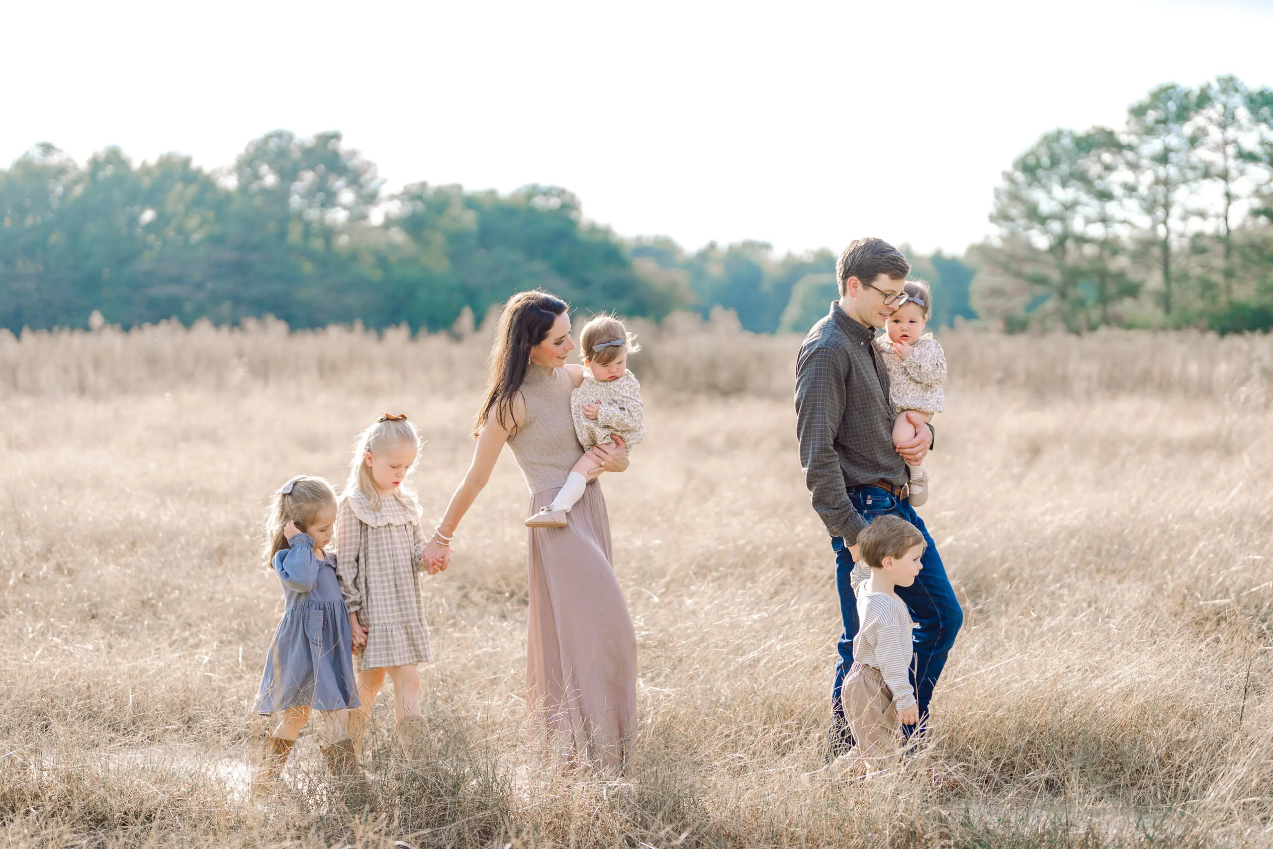 Family holding hands and walking through an open golden field during a Pinehurst NC family photo session
