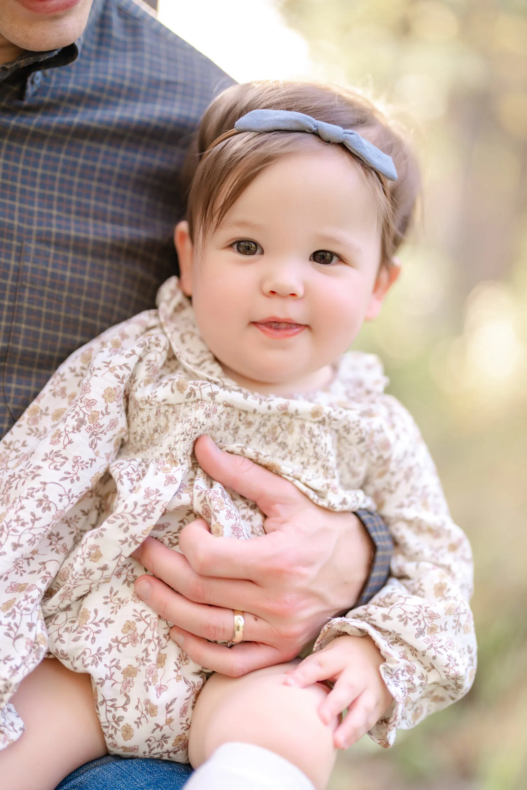Smiling baby girl in a floral dress held by her father during a Pinehurst family session