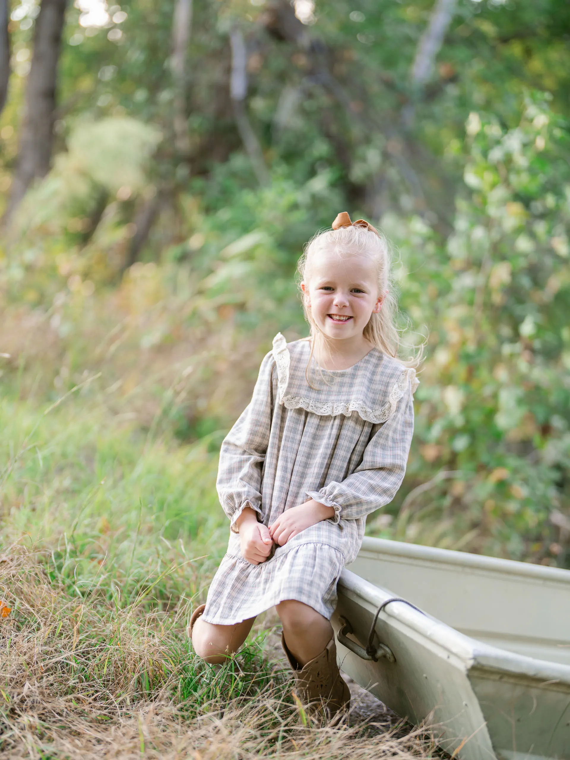 Little girl in a plaid dress sitting in a green field of tall grass