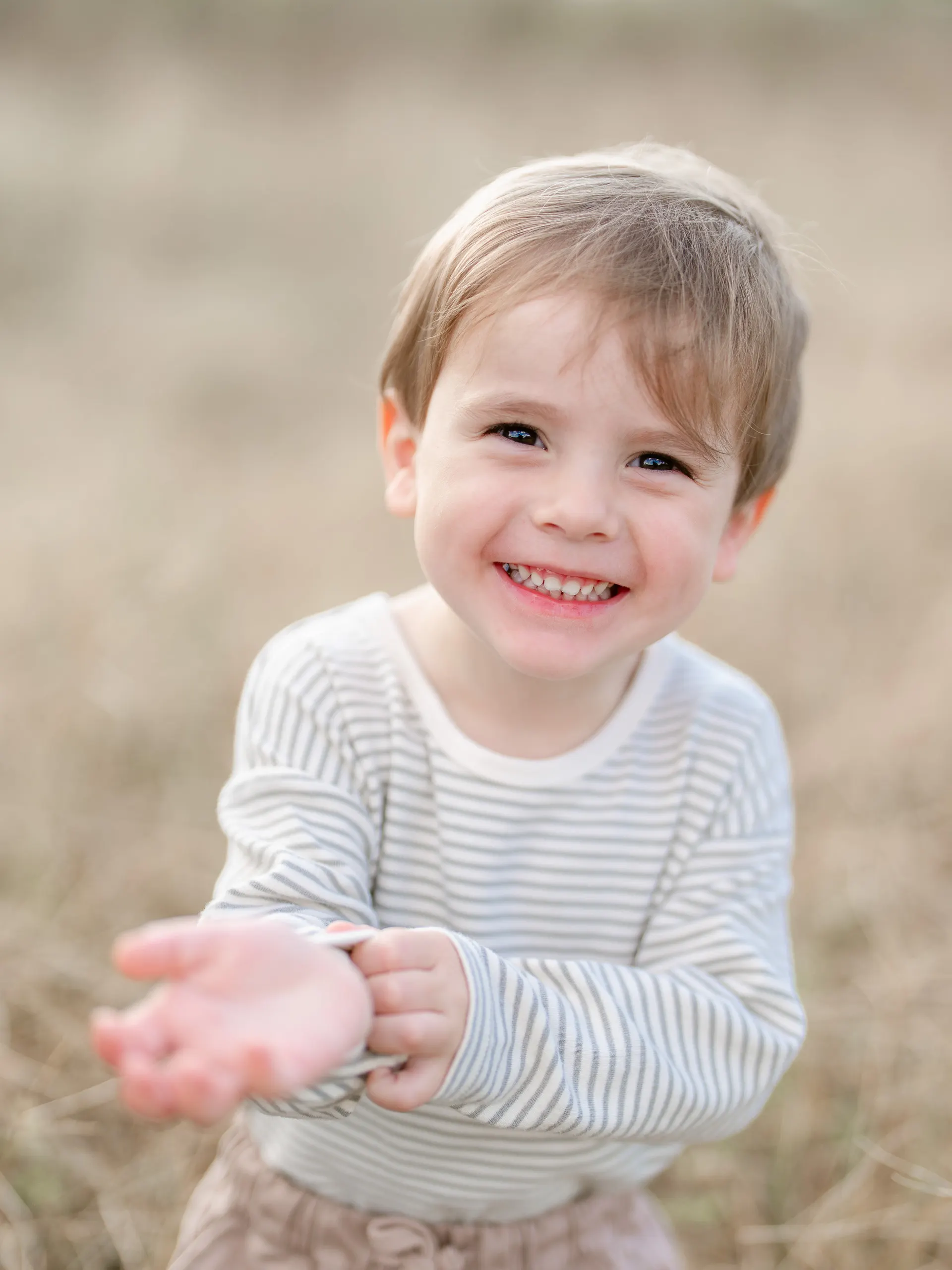 Smiling little boy in a striped sweater in tall grass