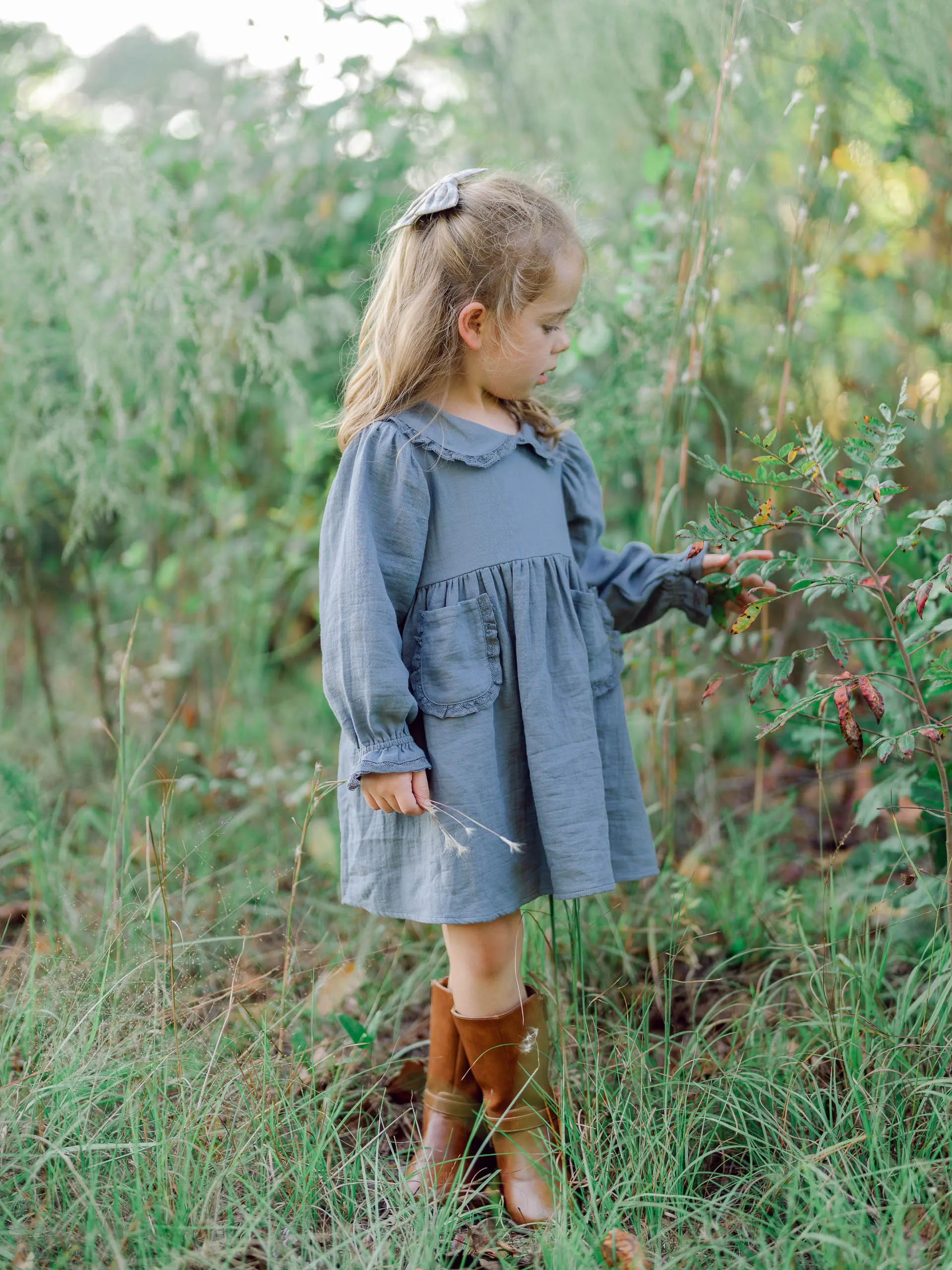 Little girl in a blue dress and boots standing in tall green grass