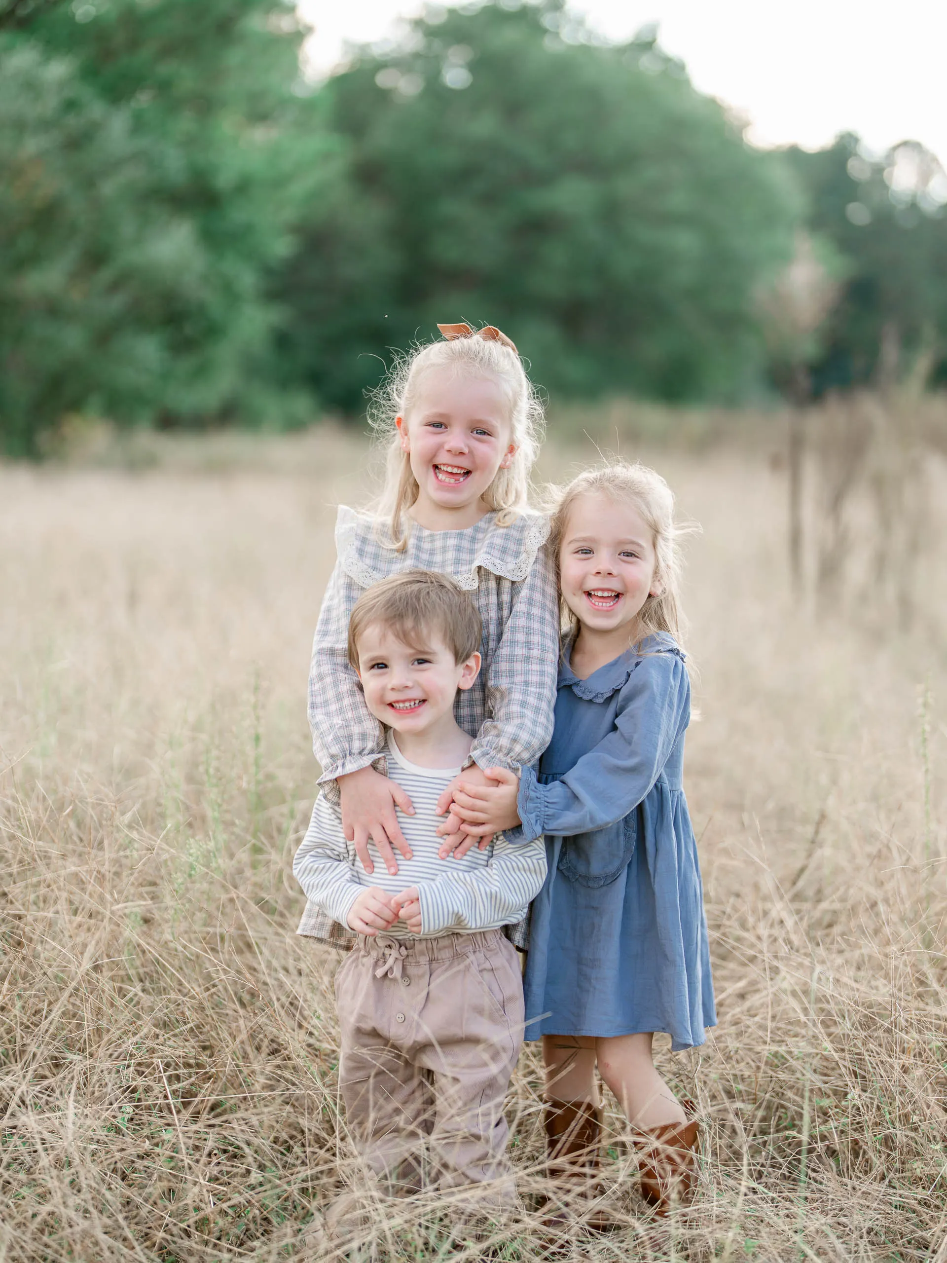 Three siblings standing close together in golden grass
