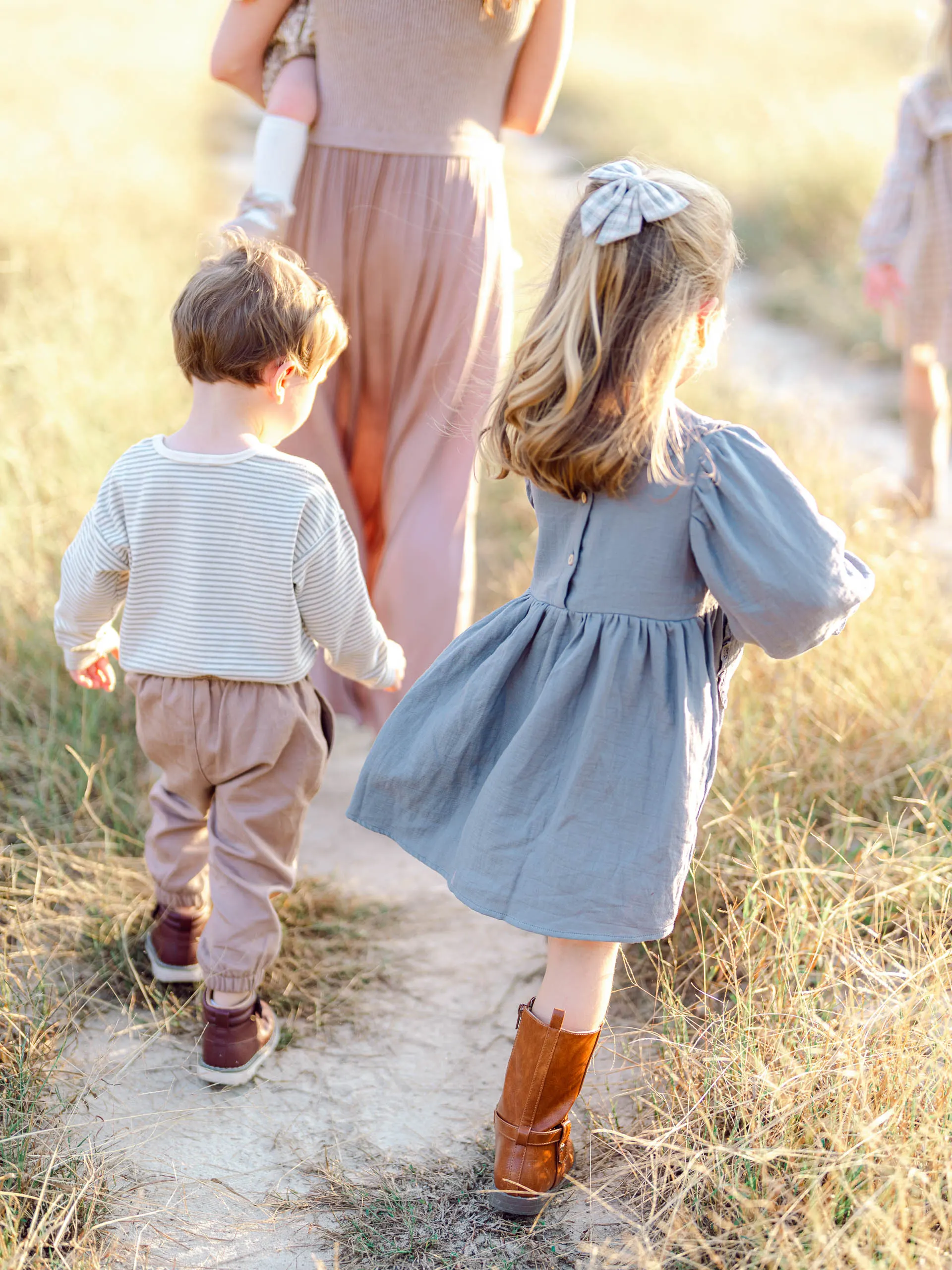 Young girl in a blue dress and a little boy walking along a sandy path in a golden field