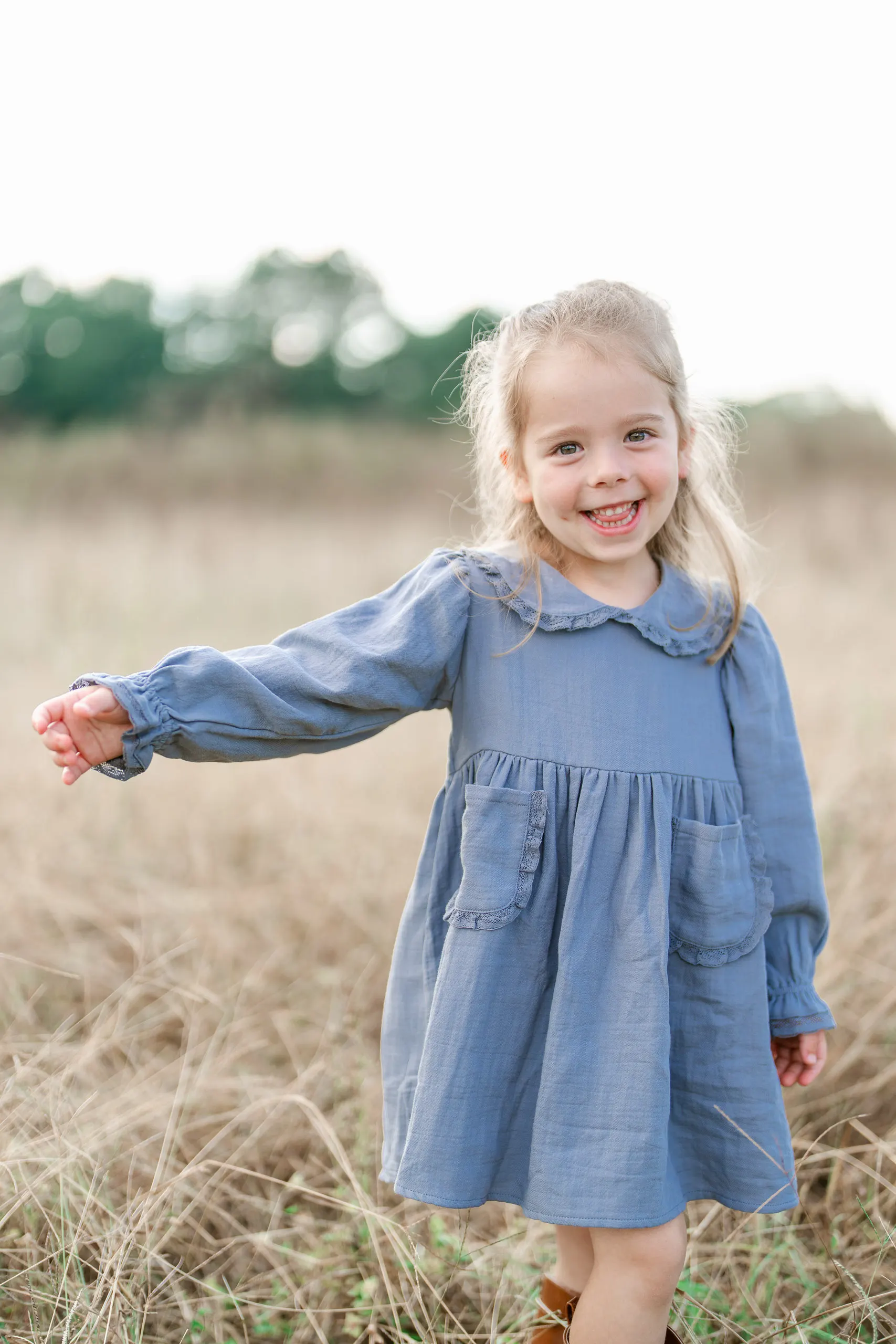 Little girl in a blue dress holding her arm out in a golden field