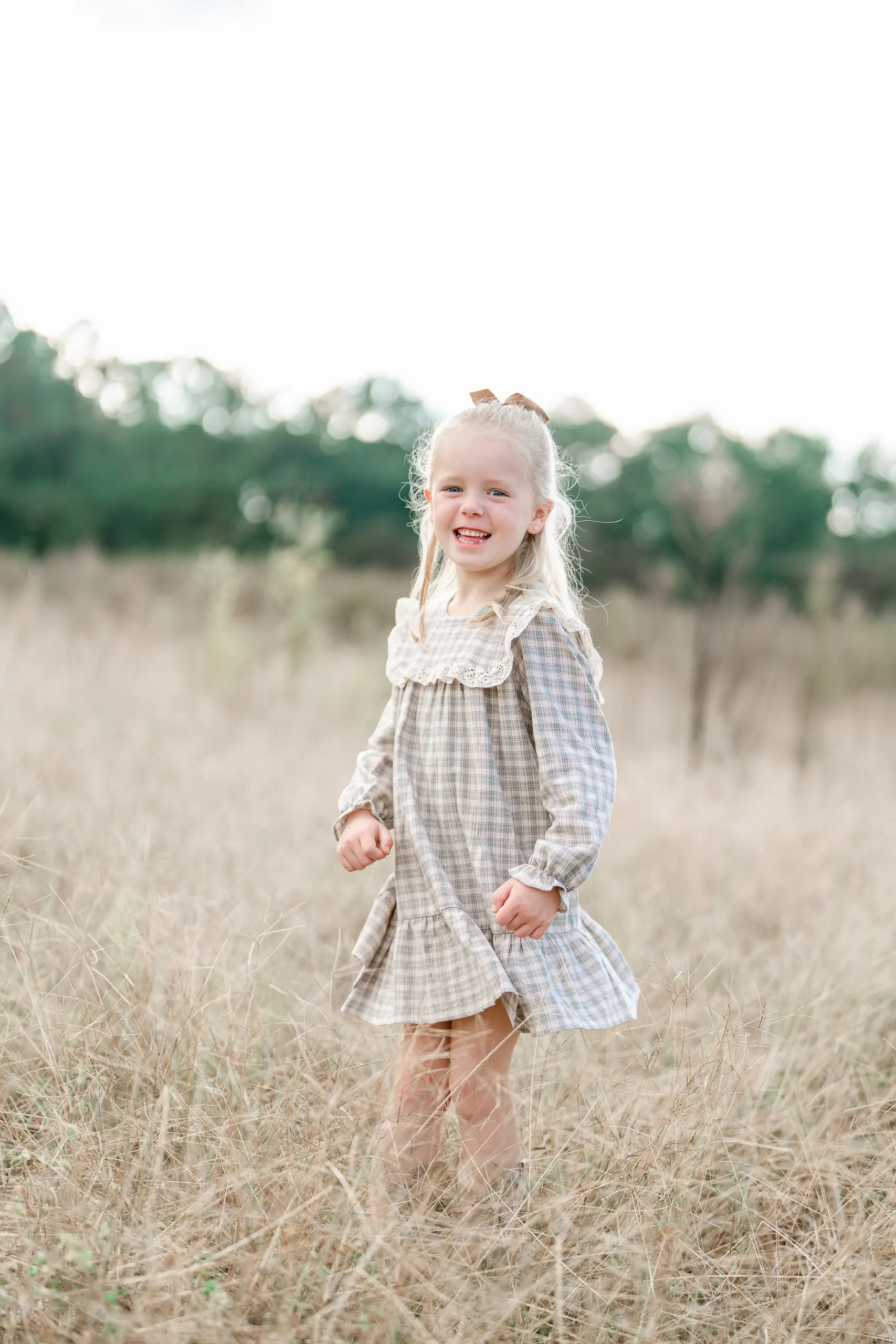 Little girl in a plaid dress standing in tall golden grass in Pinehurst NC