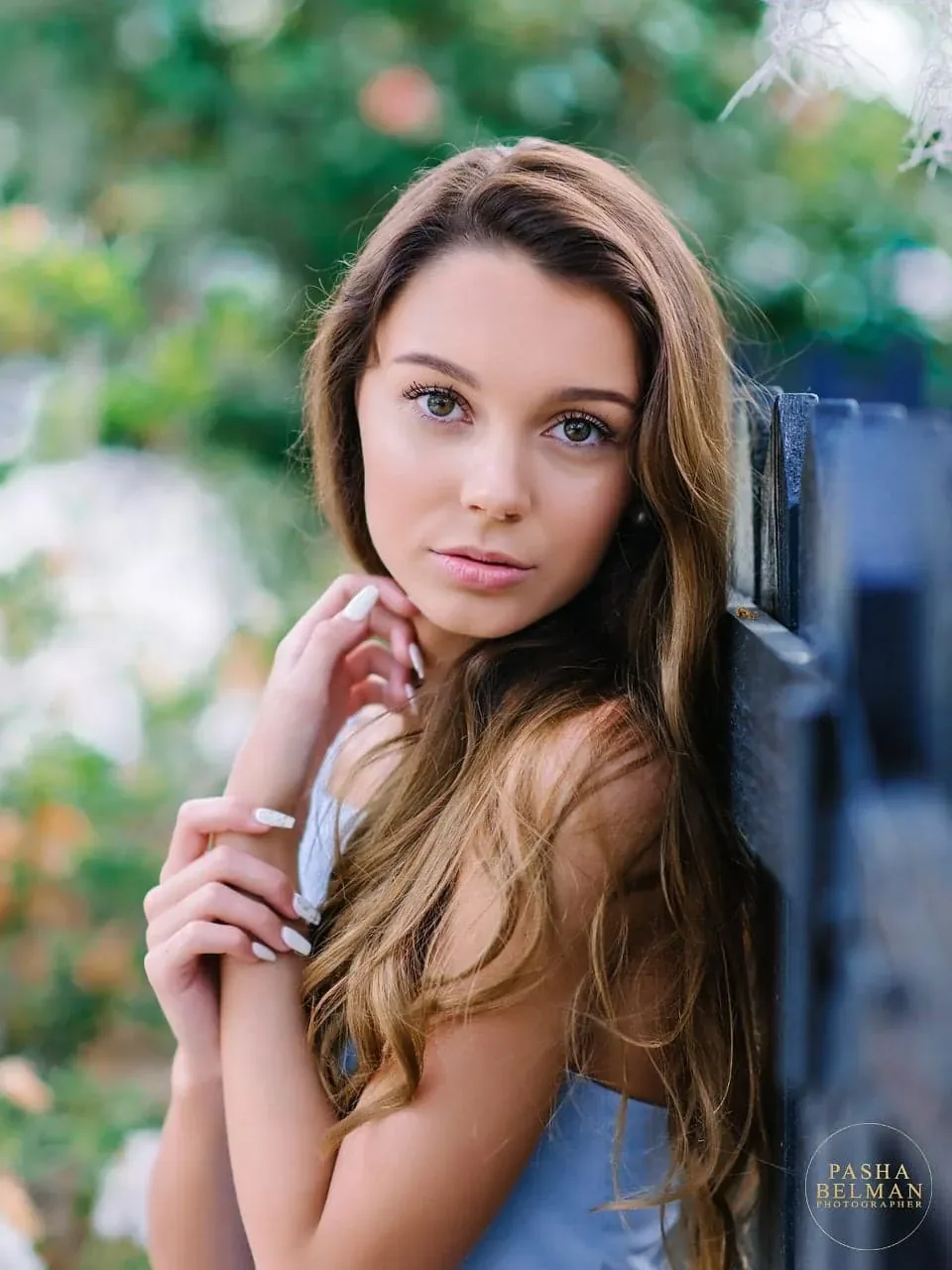 Close-up of a senior girl with long hair leaning against a wooden post in green foliage